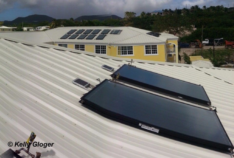 Solar thermal collectors on white corrugated roof with UVI campus buildings in background