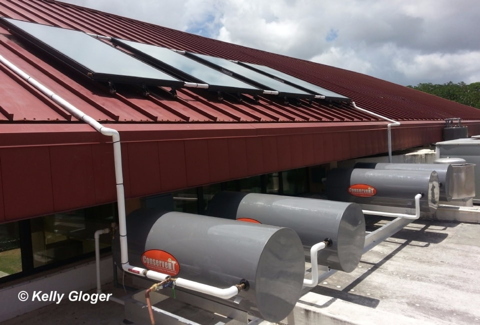 Solar hot water collectors on red metal roof with ConserveIT storage tanks below