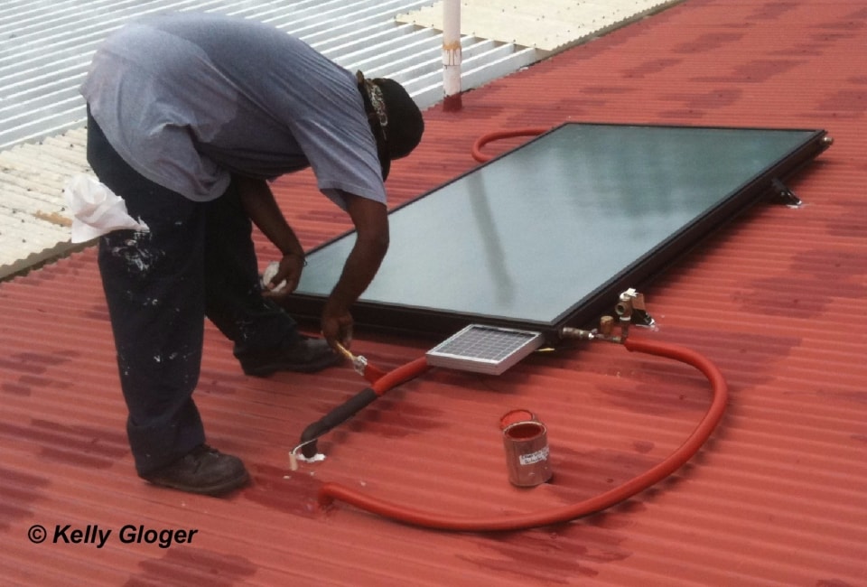 Installer working on solar hot water collector on red roof