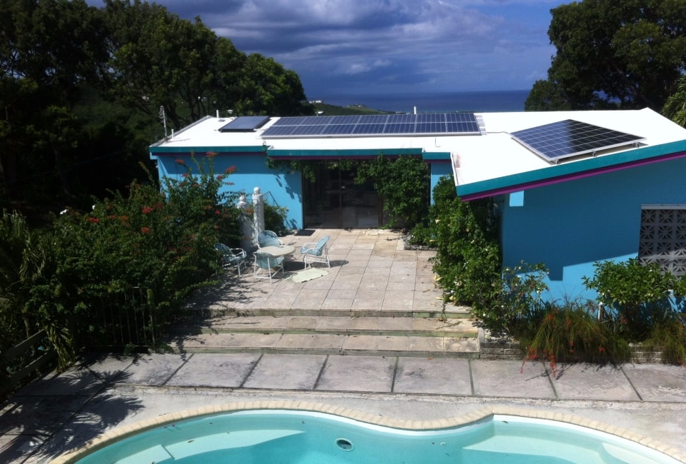 Blue residential home with solar PV panels on flat roof and pool in foreground, St. Croix USVI