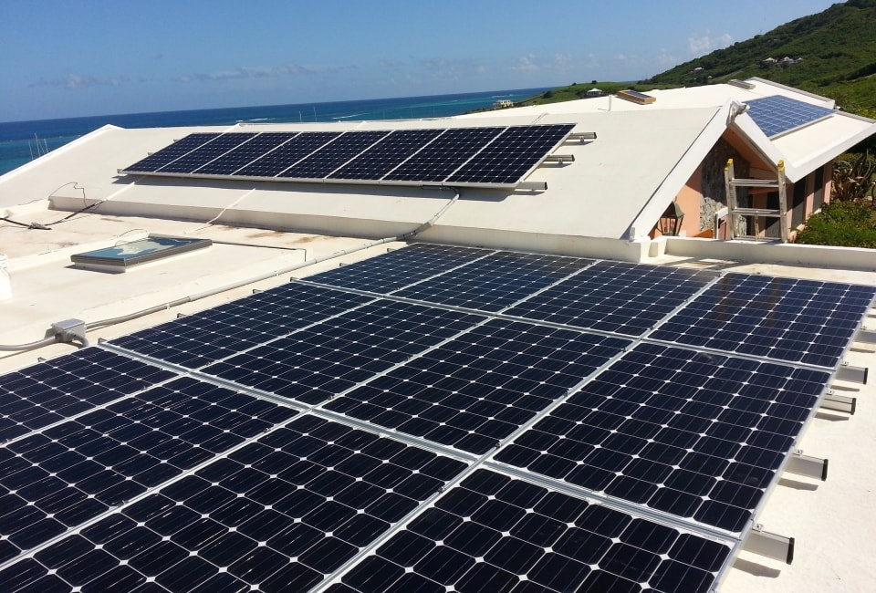 Large rooftop solar PV installation on white flat roof with Caribbean sea and green hills in background