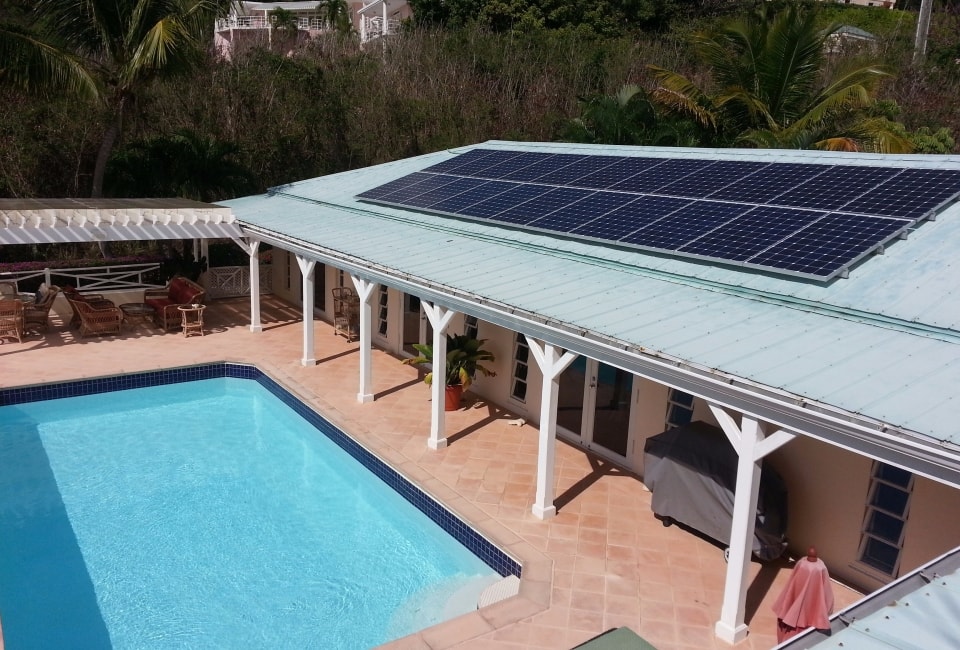 Residential home with solar PV array on green metal roof beside swimming pool with palm trees