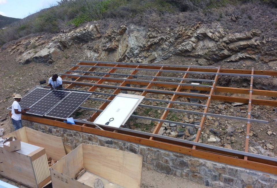 Crew installing solar PV panels on wooden racking frame against rocky hillside, St. Croix USVI