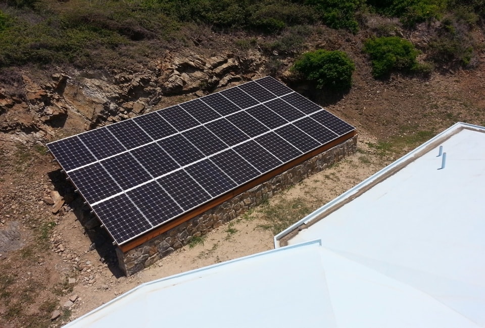 Completed ground-mount solar PV array on stone foundation against rocky hillside
