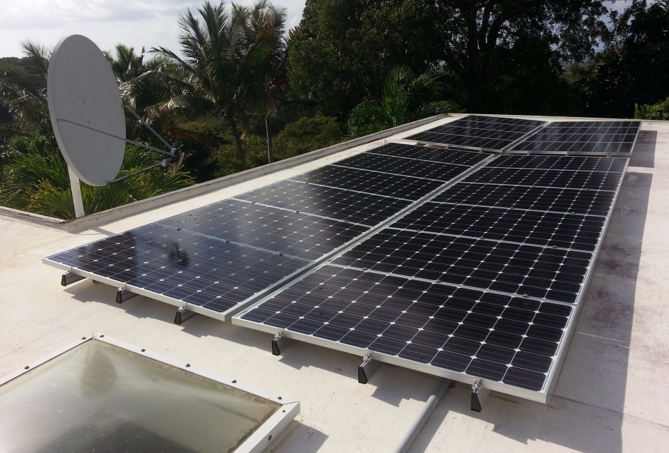 Close-up of solar PV panels on flat white roof with satellite dish and tropical vegetation