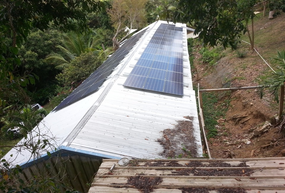 Solar PV array on long corrugated metal roof surrounded by tropical forest, St. Croix USVI